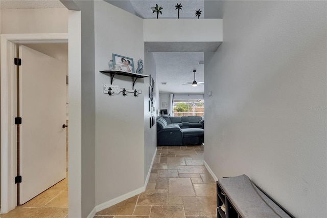 hall featuring stone tile flooring, a textured ceiling, baseboards, and a high ceiling