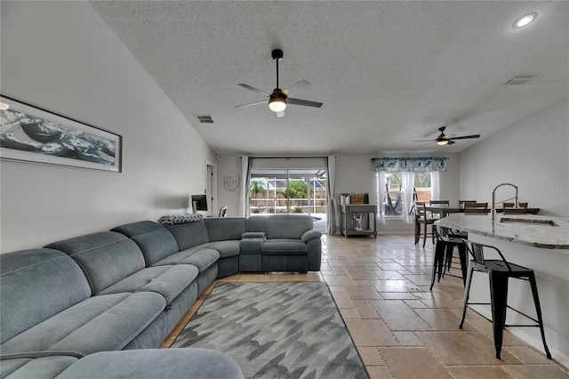 living room featuring a ceiling fan, a textured ceiling, healthy amount of natural light, stone tile flooring, and baseboards