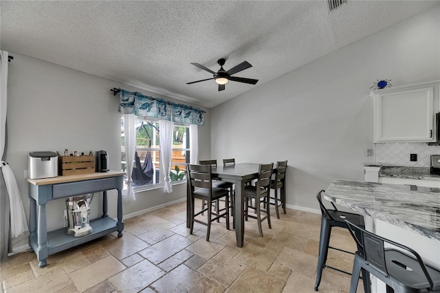 dining room with ceiling fan, a textured ceiling, stone tile flooring, and baseboards