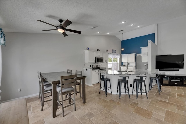 dining space featuring high vaulted ceiling, ceiling fan, a textured ceiling, stone tile floors, and baseboards