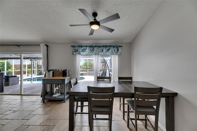 dining space with a textured ceiling, a ceiling fan, plenty of natural light, and stone tile flooring