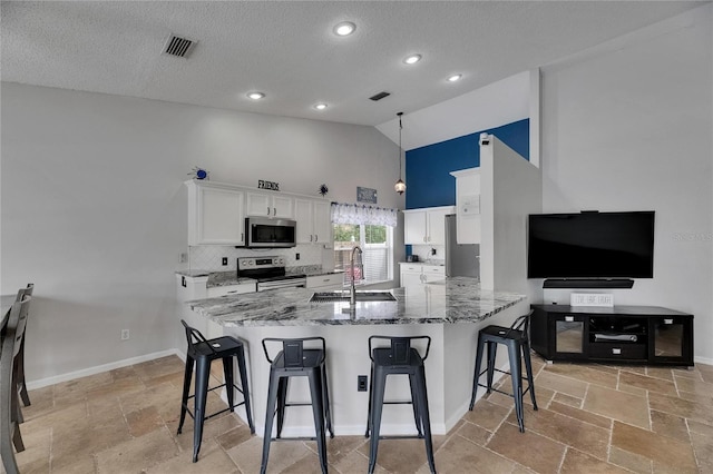kitchen featuring appliances with stainless steel finishes, high vaulted ceiling, stone tile flooring, a sink, and a breakfast bar