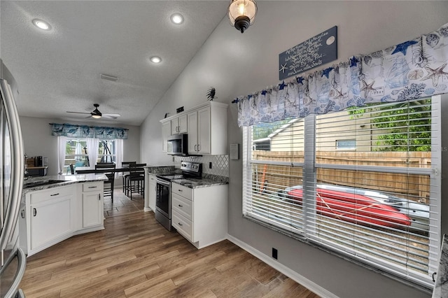 kitchen with appliances with stainless steel finishes, white cabinetry, vaulted ceiling, ceiling fan, and a textured ceiling