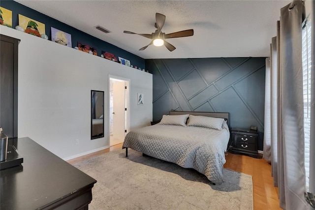 bedroom featuring a decorative wall, an accent wall, light wood-style flooring, ceiling fan, and a textured ceiling