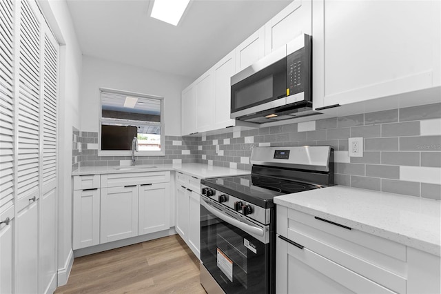 kitchen with a sink, light wood finished floors, white cabinetry, backsplash, and appliances with stainless steel finishes