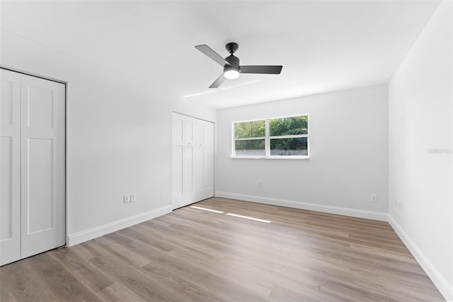 unfurnished bedroom featuring baseboards, a ceiling fan, wood finished floors, and two closets