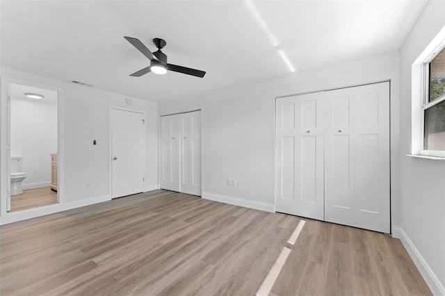 unfurnished bedroom featuring ensuite bath, multiple closets, baseboards, and light wood-style flooring