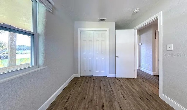 unfurnished bedroom featuring a closet, dark wood-type flooring, baseboards, and visible vents