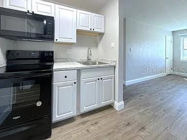 kitchen featuring white cabinetry, black appliances, light wood-style flooring, and a sink