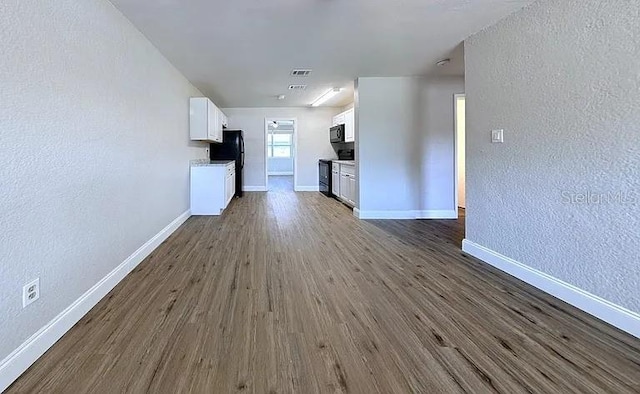 unfurnished living room featuring baseboards, dark wood-style floors, and a textured wall