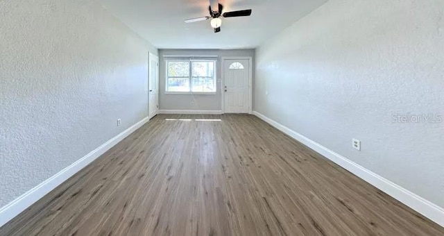 interior space featuring baseboards, wood finished floors, a ceiling fan, and a textured wall