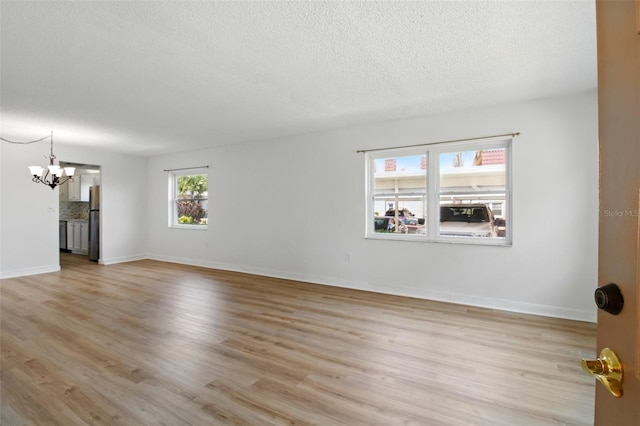 unfurnished room featuring light wood-style floors, baseboards, a notable chandelier, and a textured ceiling