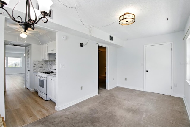 kitchen featuring white cabinets, visible vents, white range with gas cooktop, under cabinet range hood, and ceiling fan with notable chandelier
