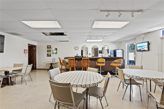 dining room featuring track lighting, baseboards, a drop ceiling, and light floors