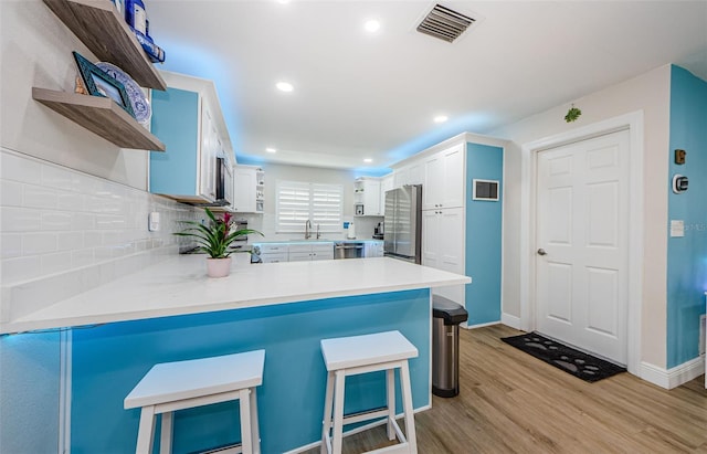 kitchen with open shelves, appliances with stainless steel finishes, light wood-type flooring, a sink, and visible vents