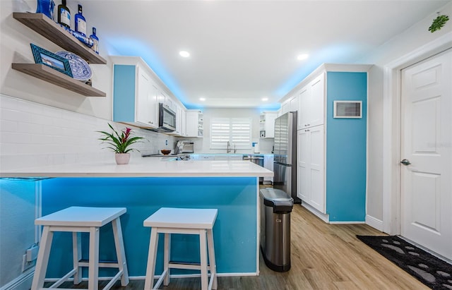 kitchen featuring a sink, stainless steel appliances, open shelves, light wood-type flooring, and a peninsula