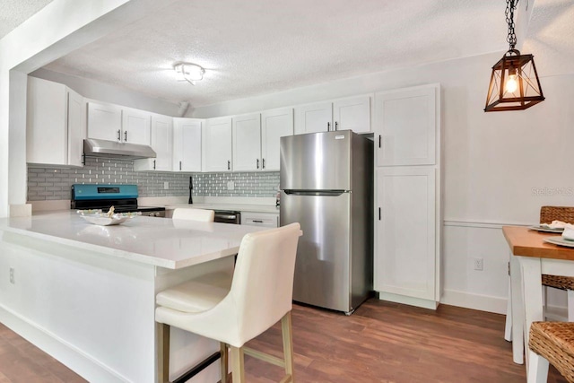 1400 Pine Glen Ln Unit B2, Tarpon Springs, FL 34688 - kitchen with under cabinet range hood, light countertops, decorative backsplash, a peninsula, and appliances with stainless steel finishes