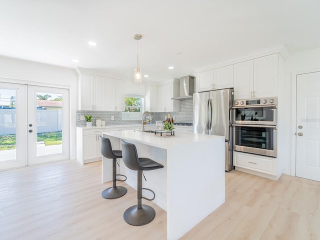 kitchen with light wood-type flooring, light countertops, appliances with stainless steel finishes, and wall chimney range hood