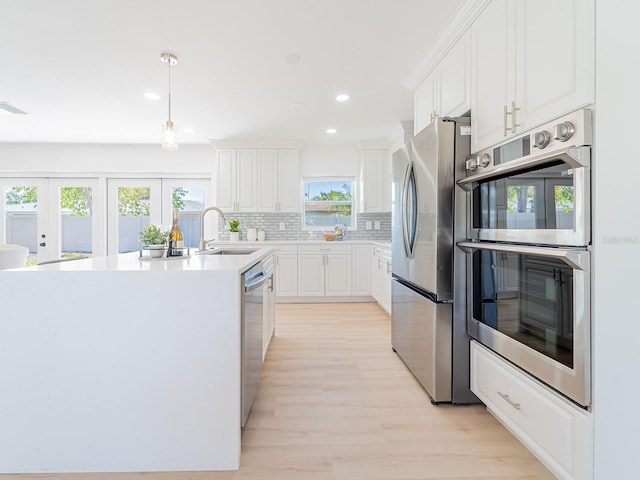 kitchen with stainless steel appliances, backsplash, a sink, light wood-style floors, and white cabinetry