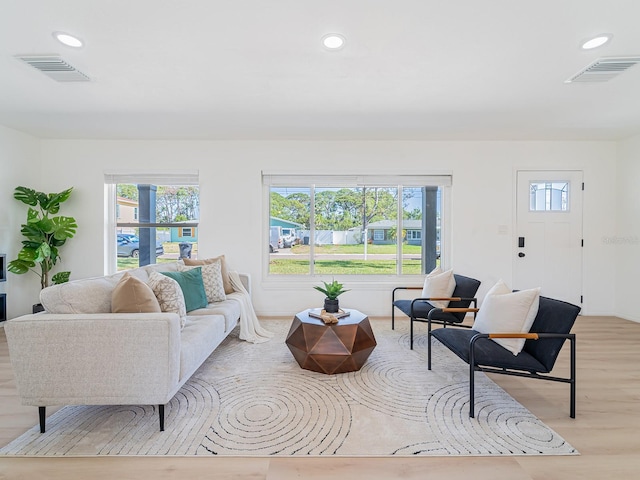 living area featuring visible vents, light wood-style floors, and a healthy amount of sunlight