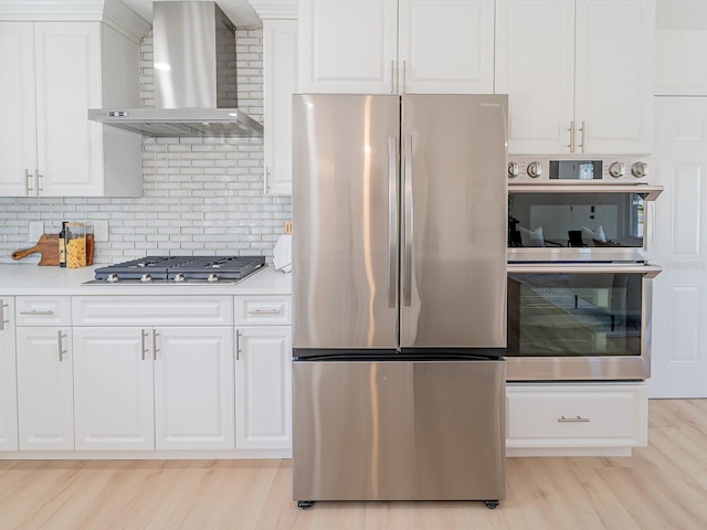 kitchen with wall chimney range hood, light countertops, white cabinetry, light wood finished floors, and appliances with stainless steel finishes