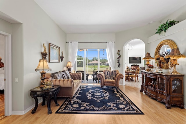 living room with arched walkways, baseboards, and light wood-type flooring