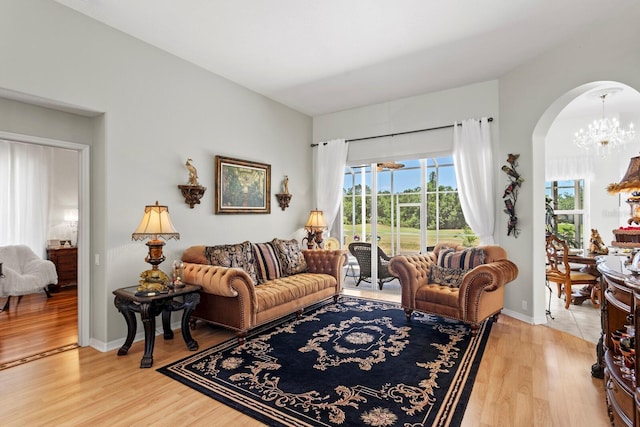 living area with baseboards, arched walkways, a notable chandelier, and light wood finished floors