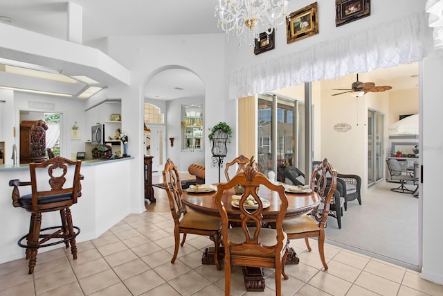 dining area featuring light tile patterned floors, arched walkways, and ceiling fan with notable chandelier
