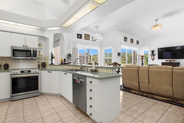 kitchen featuring a sink, an inviting chandelier, tasteful backsplash, a peninsula, and appliances with stainless steel finishes