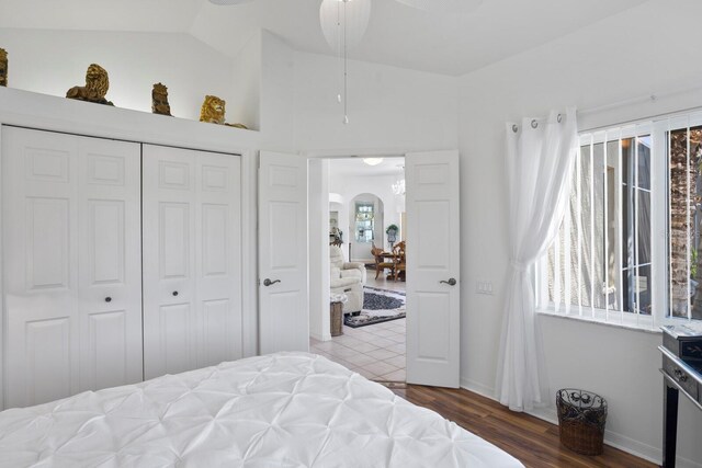 bedroom featuring arched walkways, a closet, wood finished floors, and baseboards