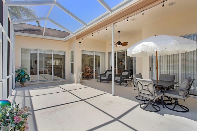 view of patio featuring ceiling fan, glass enclosure, and outdoor dining area