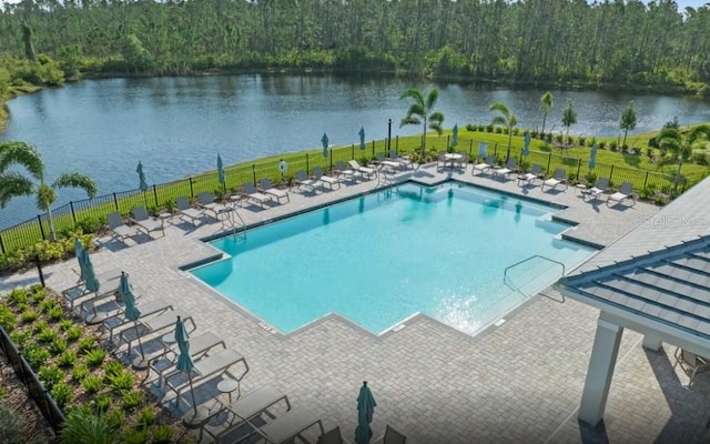 community pool with a wooded view, a patio, a water view, and fence