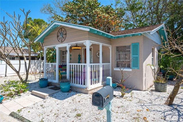 view of front of property with fence, covered porch, stucco siding, and a shingled roof