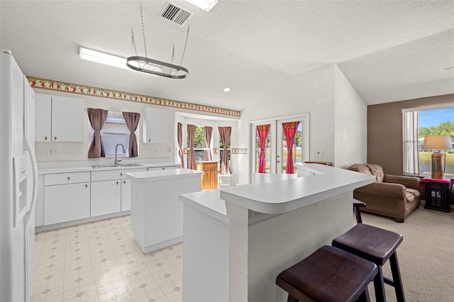 kitchen featuring a kitchen island, a sink, light countertops, white fridge with ice dispenser, and a breakfast bar