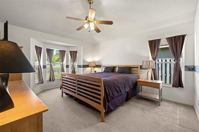 carpeted bedroom with baseboards, a textured ceiling, ceiling fan, and multiple windows