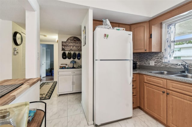 9945 47th Ave N Unit 208, Saint Petersburg, FL 33708 - kitchen with freestanding refrigerator, a sink, light marble finish flooring, backsplash, and brown cabinetry