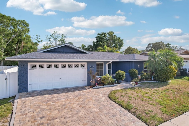 ranch-style house featuring decorative driveway, a garage, and fence