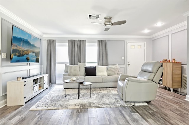 living area with ceiling fan, crown molding, visible vents, a decorative wall, and wood finished floors