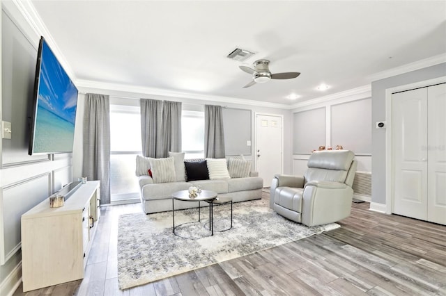 living area with wood finished floors, crown molding, visible vents, a decorative wall, and a ceiling fan