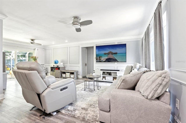 living area featuring wood finished floors, a decorative wall, ceiling fan, and crown molding