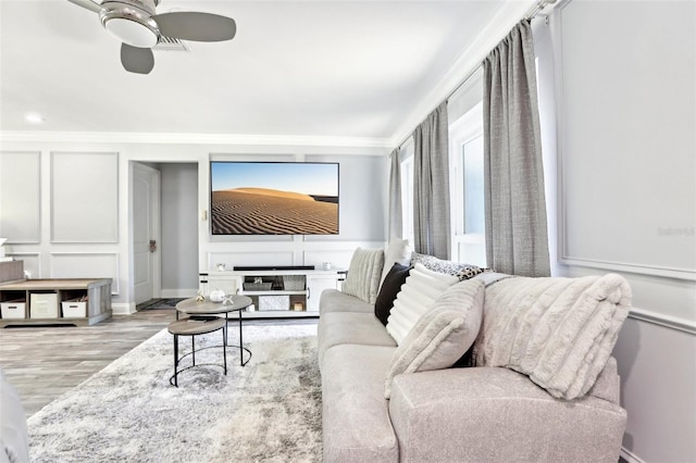 living area featuring wood finished floors, a ceiling fan, crown molding, and a decorative wall