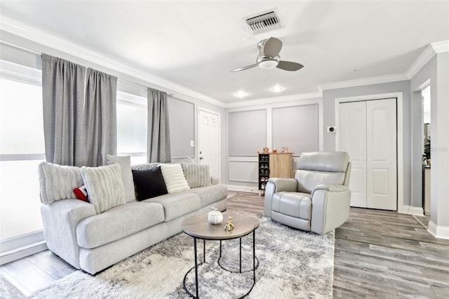 living area with crown molding, visible vents, ceiling fan, baseboards, and wood finished floors
