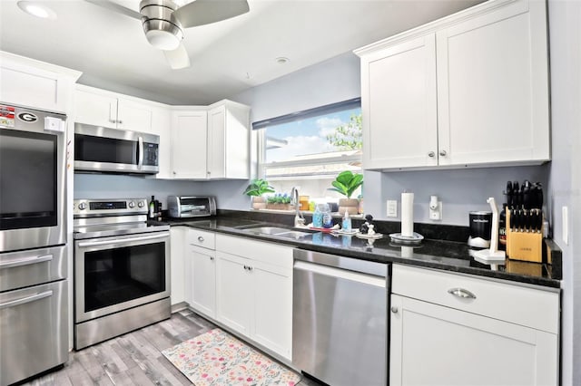 kitchen featuring white cabinets, stainless steel appliances, light wood-style floors, and a sink