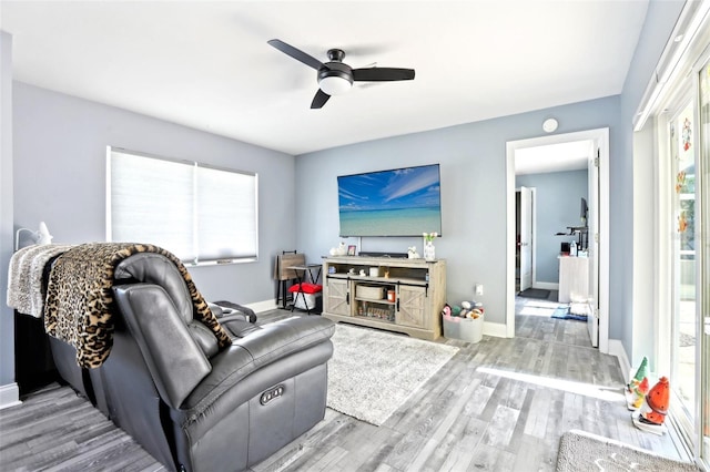 living area featuring wood finished floors, a healthy amount of sunlight, a ceiling fan, and baseboards