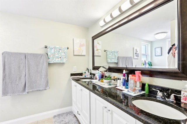 bathroom with baseboards, tile patterned floors, double vanity, and a sink