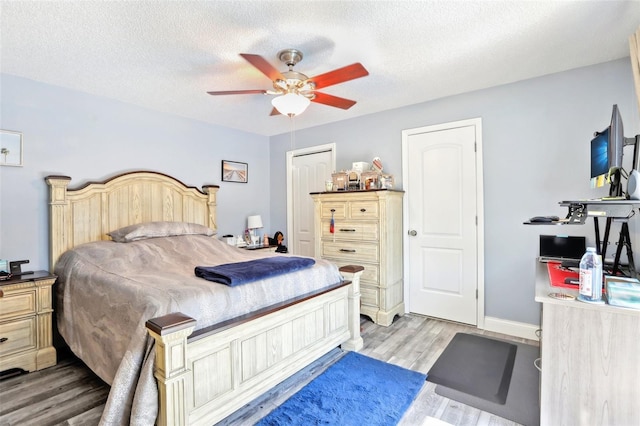 bedroom with a closet, ceiling fan, light wood-style flooring, baseboards, and a textured ceiling