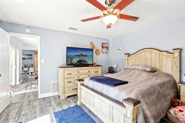 bedroom featuring a textured ceiling, visible vents, a ceiling fan, and light wood-style flooring