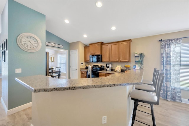 kitchen featuring light wood finished floors, vaulted ceiling, baseboards, black appliances, and a breakfast bar area