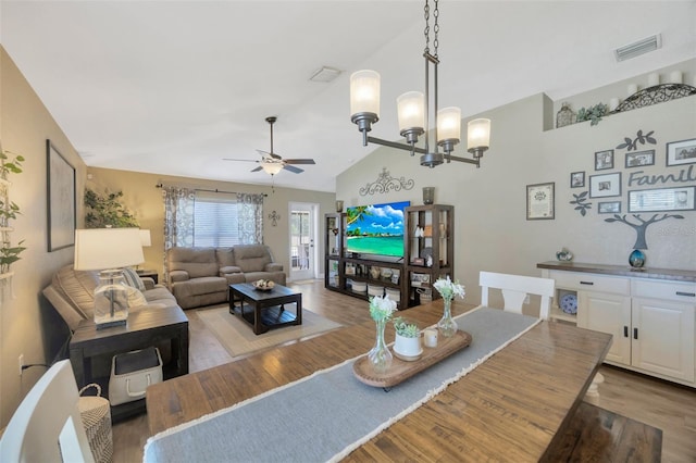 dining area with ceiling fan with notable chandelier, light wood-style flooring, visible vents, and high vaulted ceiling