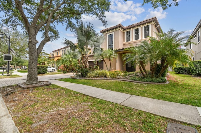 mediterranean / spanish house with a front lawn, stucco siding, and a tiled roof